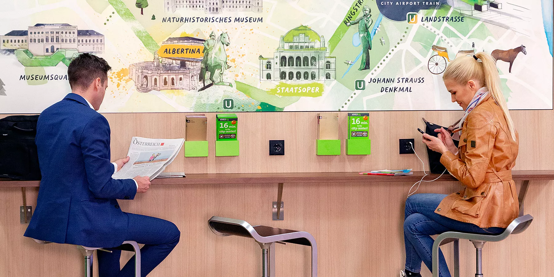 Herr in Wien Mitte sitzt mit einer Mitarbeiterin der City Airport Train vor einer Wien-Karte im CAT-Foyer_C-CAT Hammerschmid