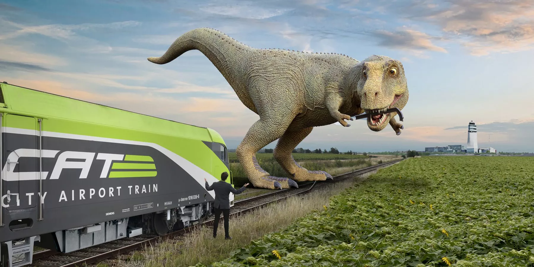 Ein Dinosaurier steht auf den Gleisen vor einem City Airport Train Lokomotive_C-CAT